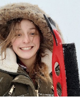 Alyssa Koktavy smiles with a fuzzy winter hood over her head and a snow scraper in her hand