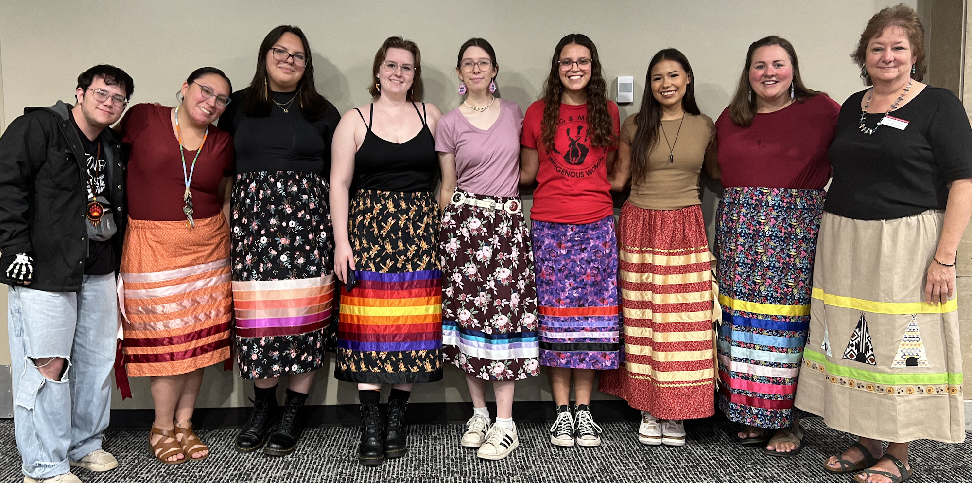 Line of 9 students and faculty, many in colorful ribbon skirts, at the 2023 fall feast
