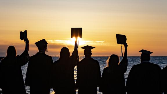 Graduates lifting their caps as they watch the sun rise over lake superior 