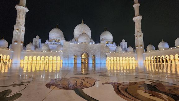 Sheikh Zayed Grand Mosque, a nighttime photo of the impressively large building featuring white marble domes and towers.