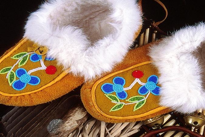 pair of tan moccasins with fuzzy insides and blue beaded flowers on the tops