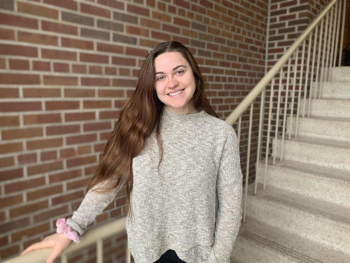 Abby Shelby, smiling, standing on stairs with a brick wall in the background
