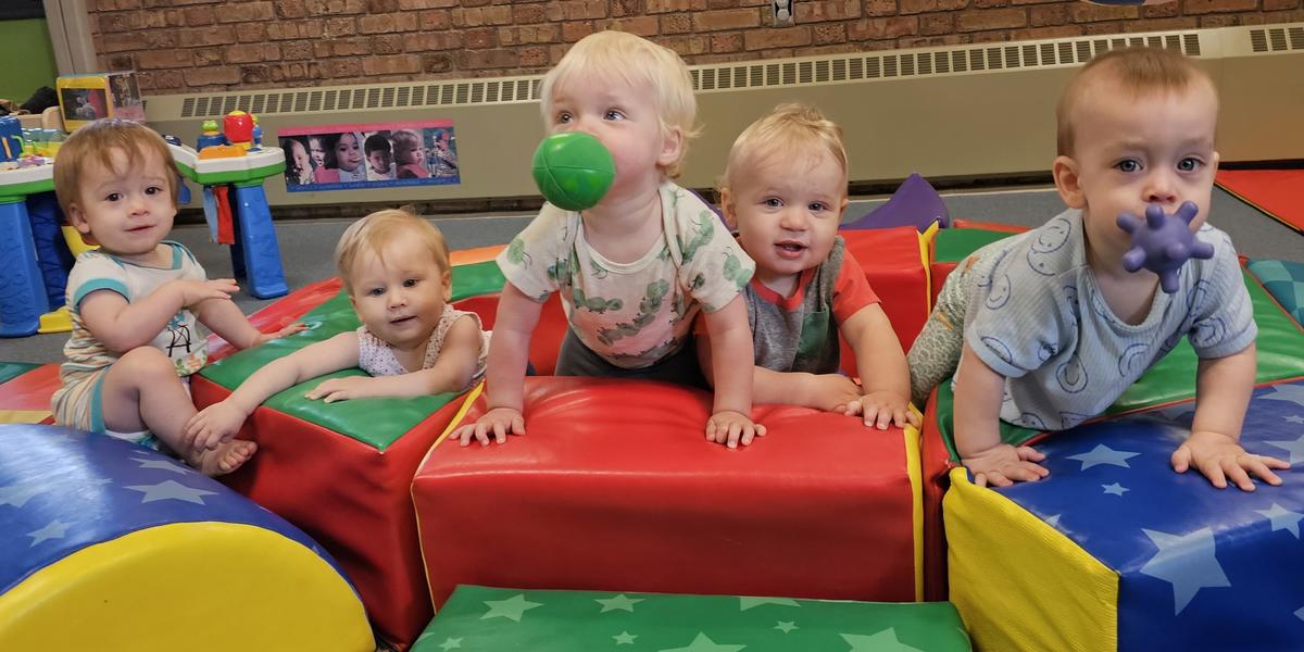 group of infants crawling over play blocks with colorful toys in their mouths 
