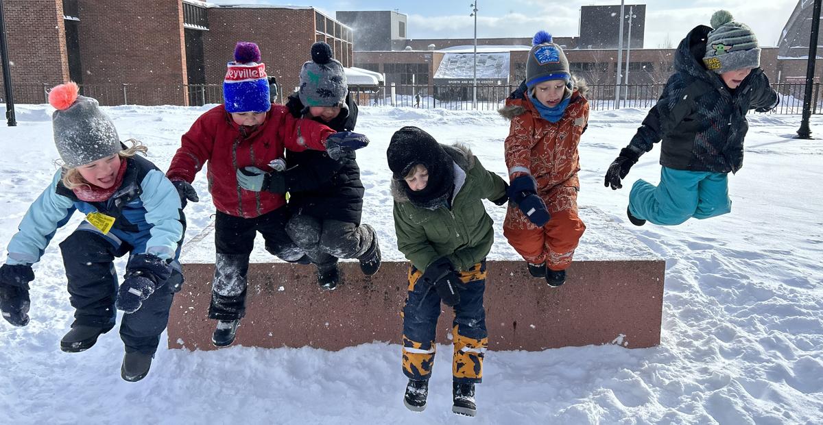 group of preschoolers excitedly jumping off a short ledge into snow 