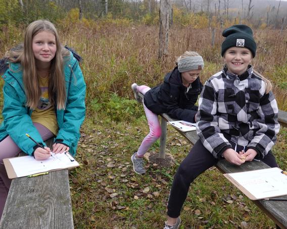 Three students at Lakewood Elementary writing field observations from their school forest
