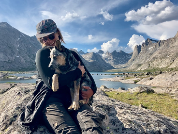 Simone Anzion hugs a dog in a mountainous outdoor location