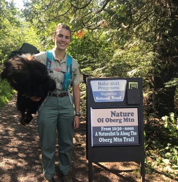 Elizabeth ross holding fur in front of a sign that reads "Naturalist programs Superior National Forest"