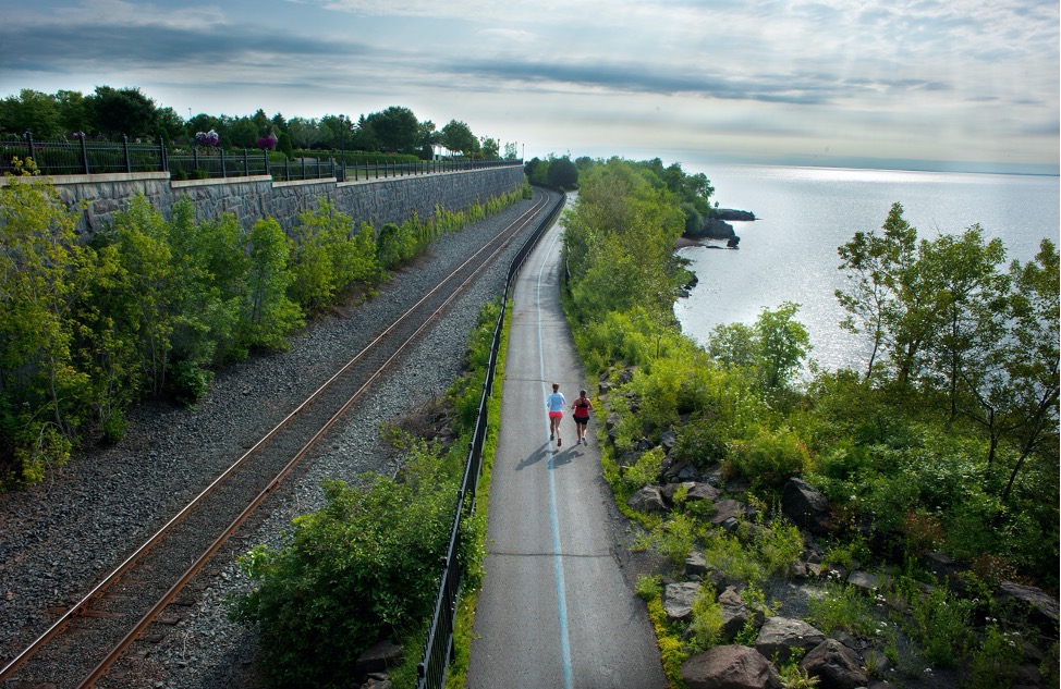 Rear aerial view of 2 joggers on the Lakewalk trail next to Lake Superior