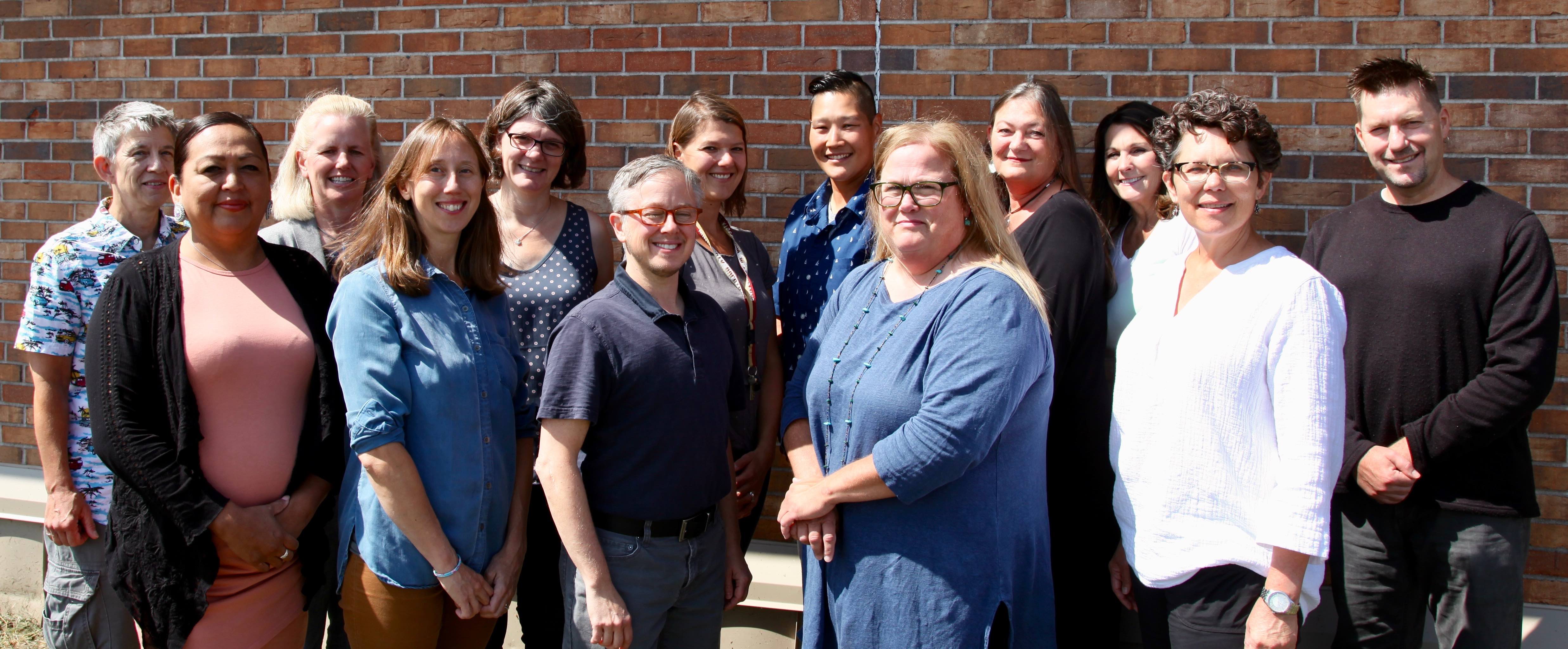 Social Work department faculty and staff posing in front of a brick wall on a sunny day