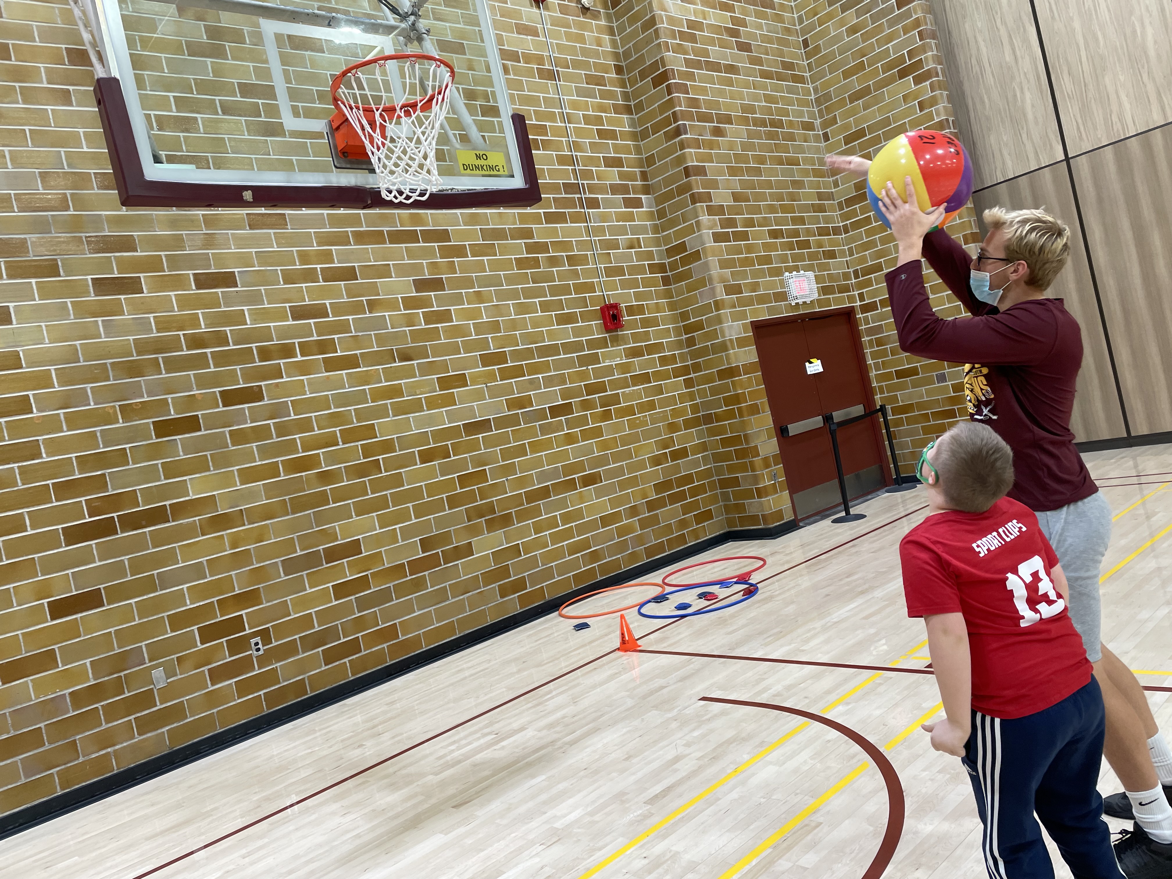 college student using a beach ball to show a young child how to shoot the ball into a basketball hoop