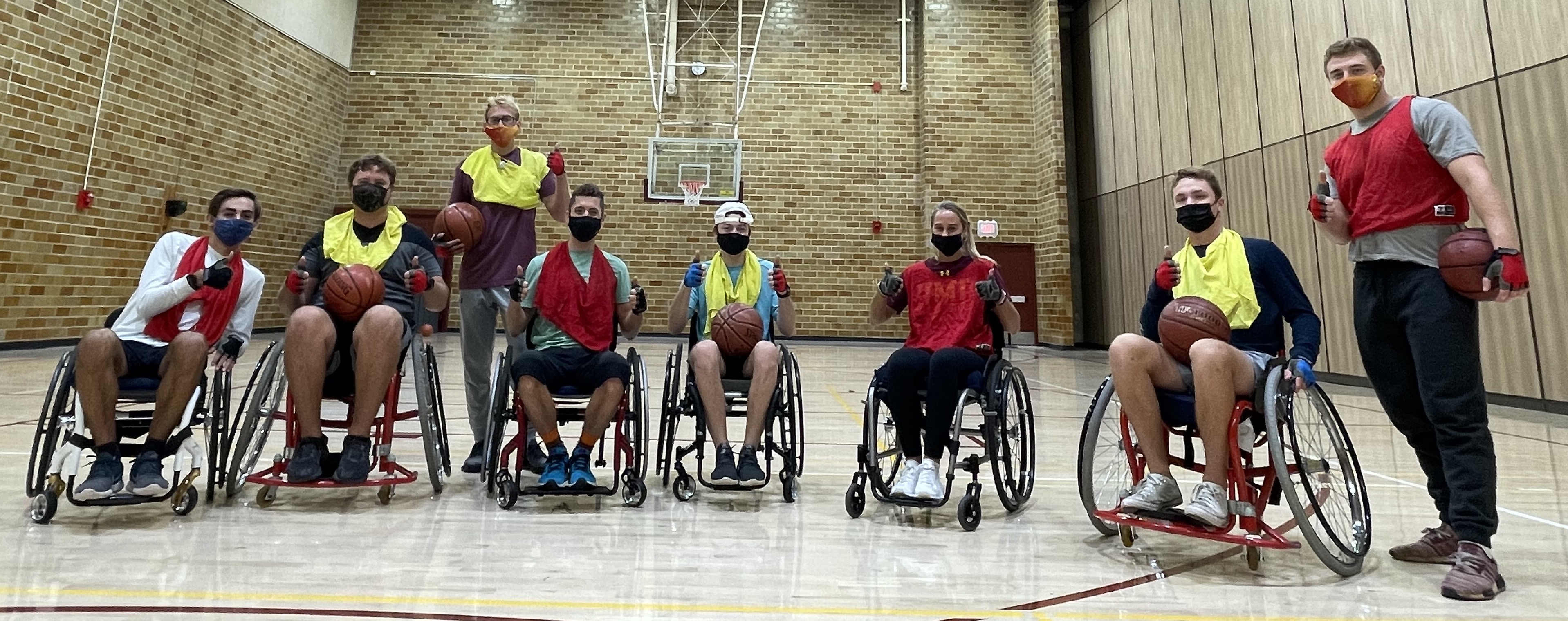 several people in wheelchairs playing basketball, facing the camera and giving a thumbs up