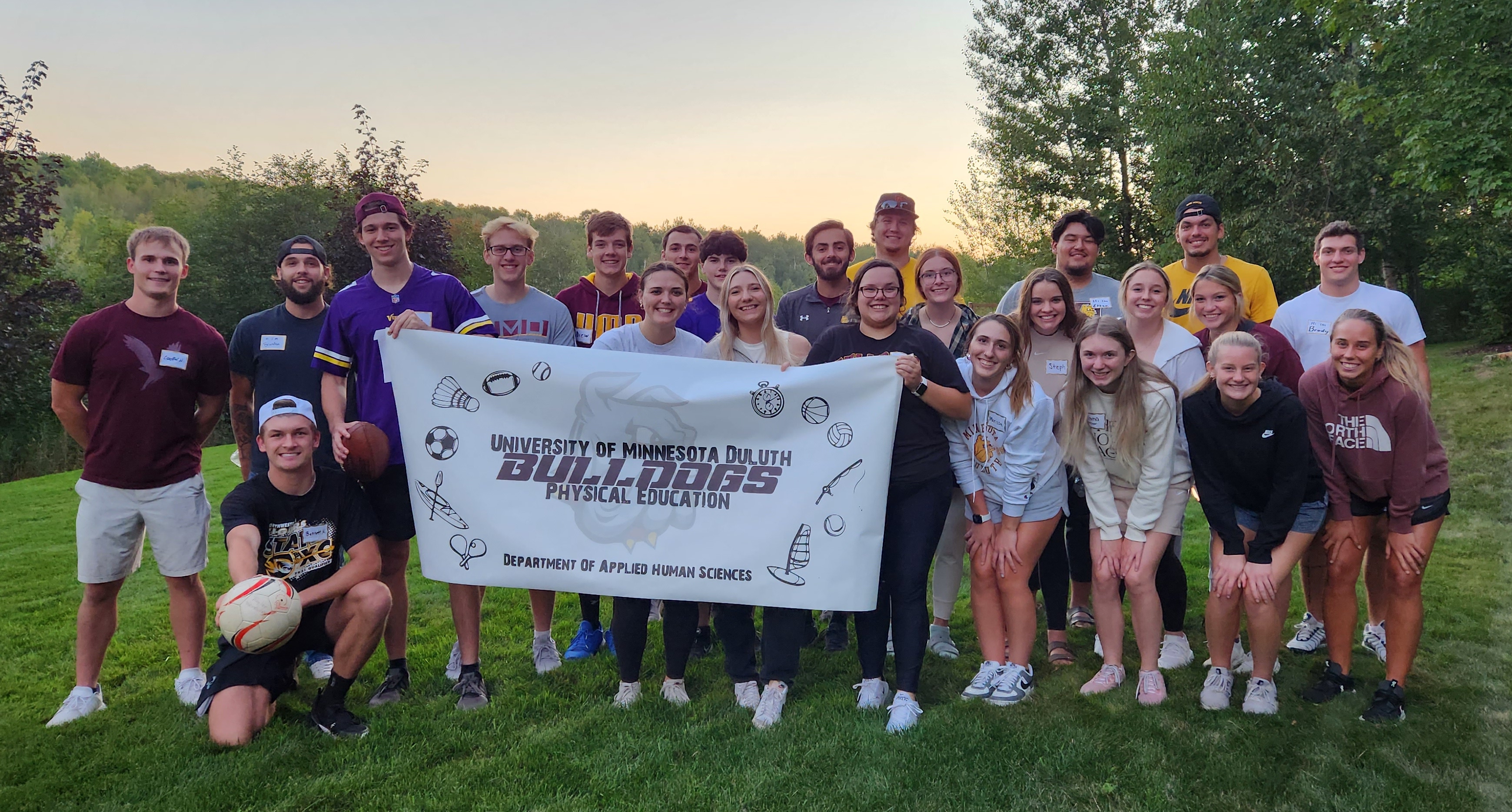 24 college students smiling and posing while holding a sign that reads University of Minnesota Duluth Bulldogs Physical Education