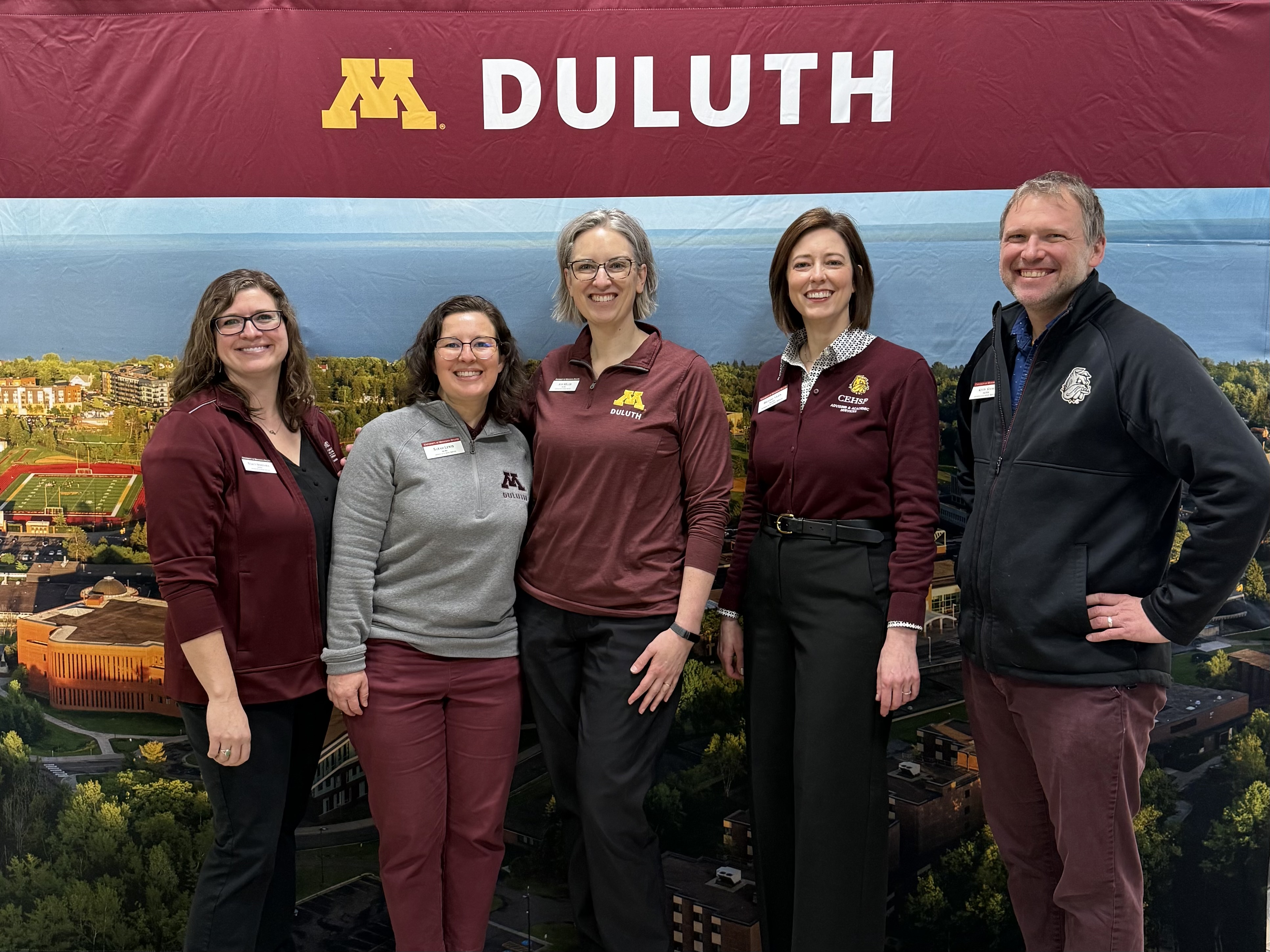 4 women and 1 man standing in front of an M Duluth sign