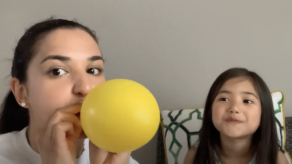 Woman blowing up a yellow balloon as child looks on