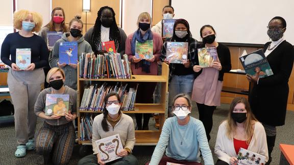 Group of students and faculty, masked and holding children's books