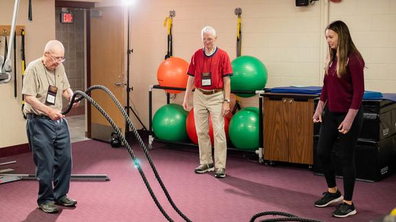 two older adults learning to use ropes with student looking on