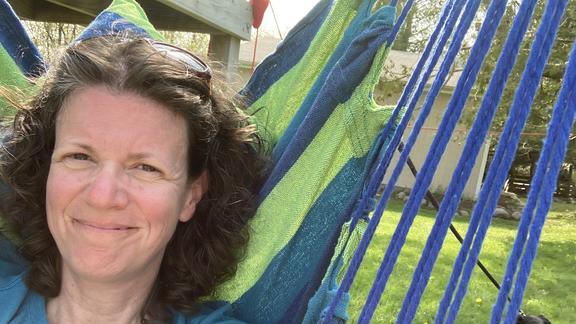 Jennifer Frisch, smiling in a hammock with a black dog laying on the grass in the background
