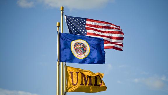 3 flags in the wind: United States of America, Minnesota, and UMD.