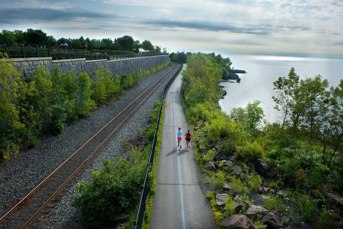 Rear aerial view of 2 joggers on the Lakewalk trail next to Lake Superior