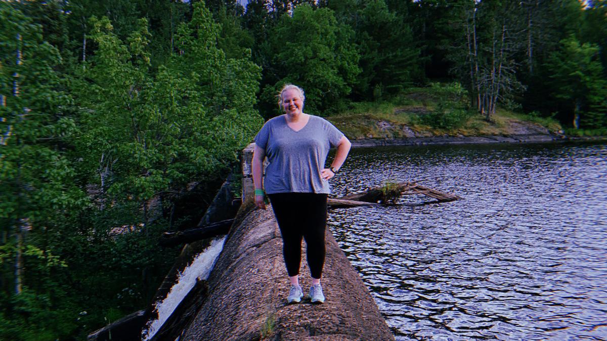 Gabby Suihkonen stands on a dam with water and trees in the background