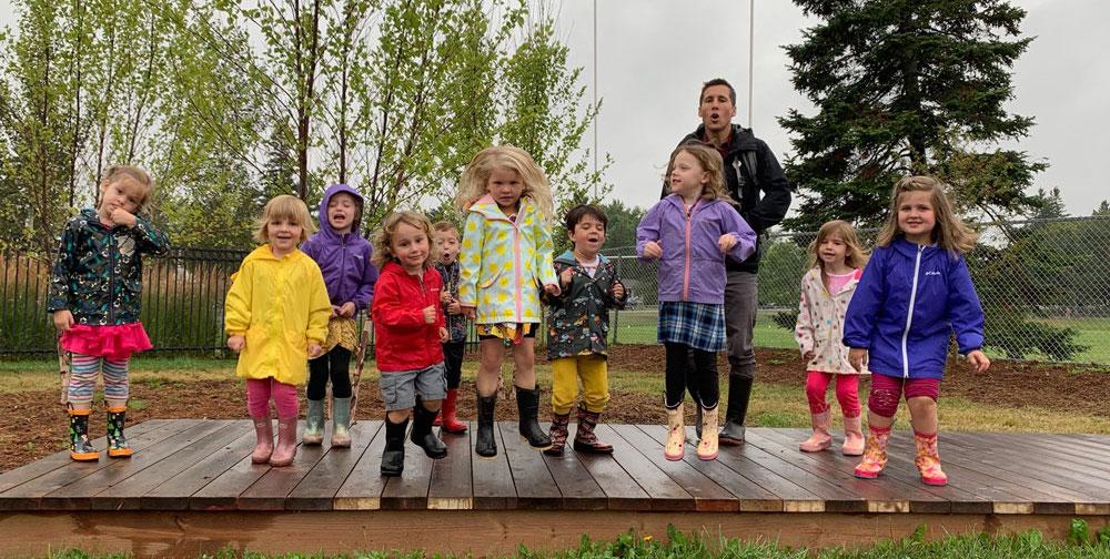 preschoolers dressed in rain coats and boots jumping on a wood platform