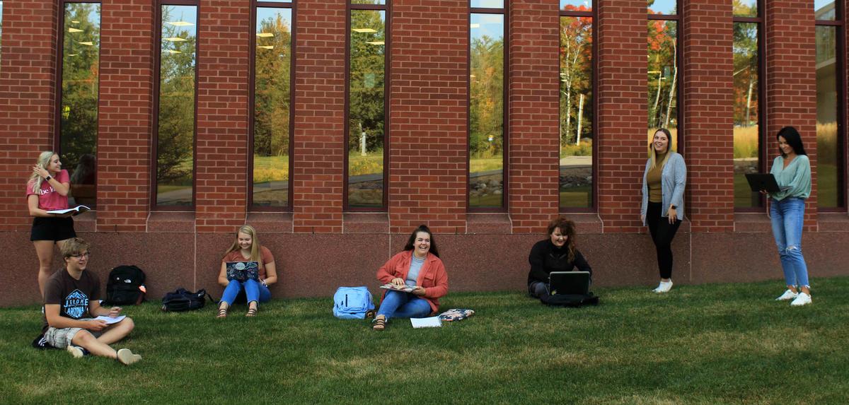 7 students spaced apart standing/sitting outside UMD library