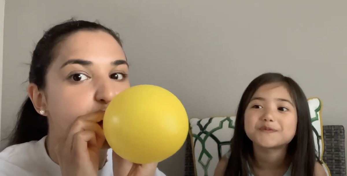 Woman blowing up a yellow balloon as child looks on