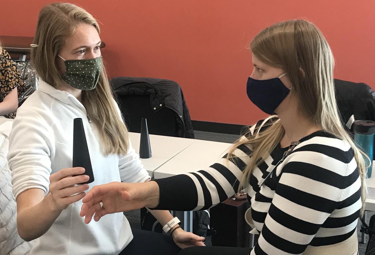 Two students wearing masks, looking at one another, performing a test of coordination