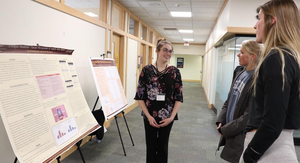 Student smiling and presenting her poster to two other students