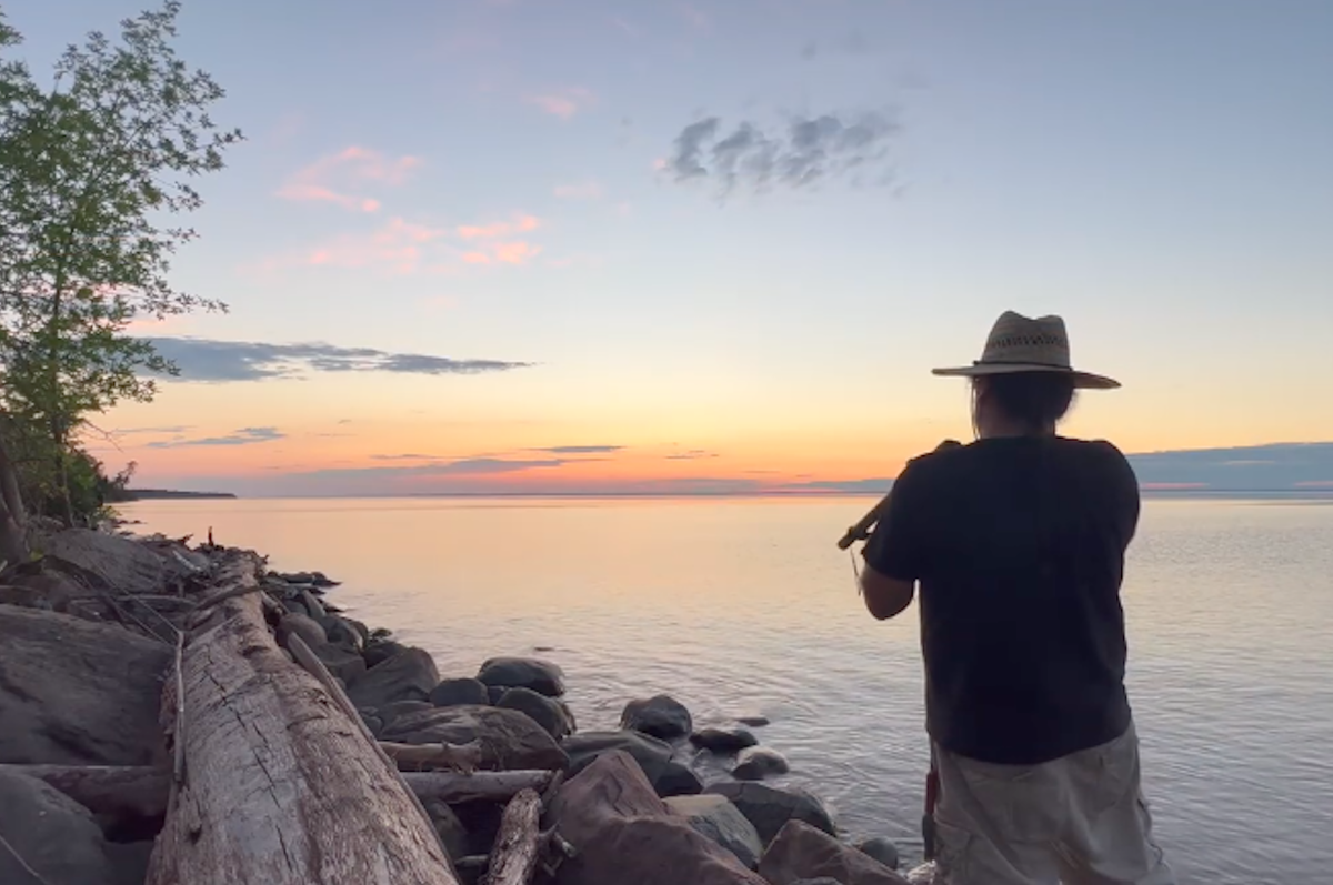 sunset over a lake with a person playing a flute