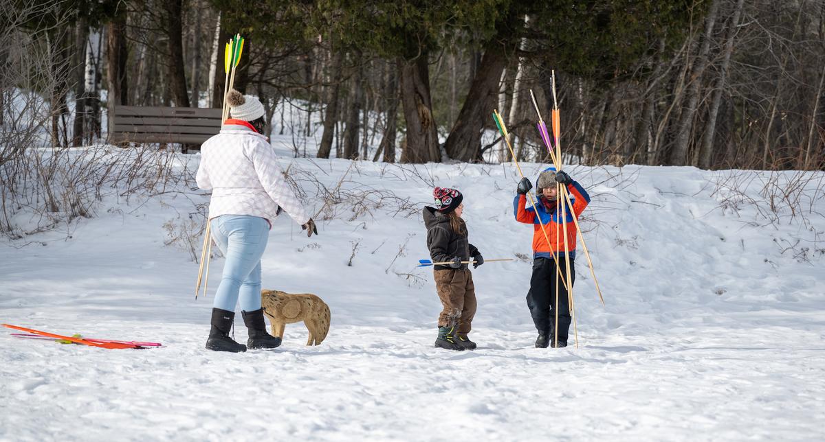 Two children and an adult outside in the snow with atlatl spear game