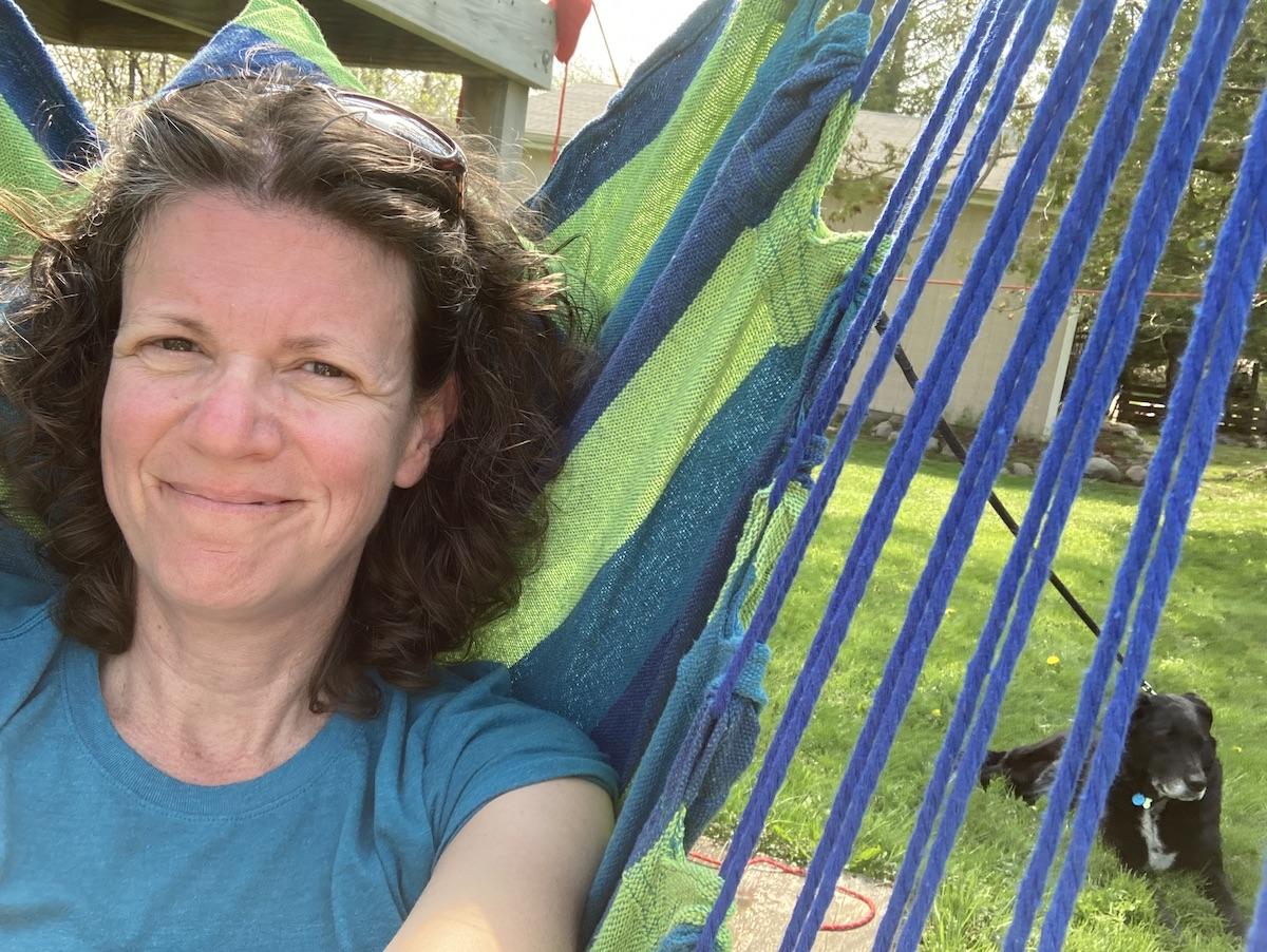 Jennifer Frisch, smiling in a hammock with a black dog laying on the grass in the background