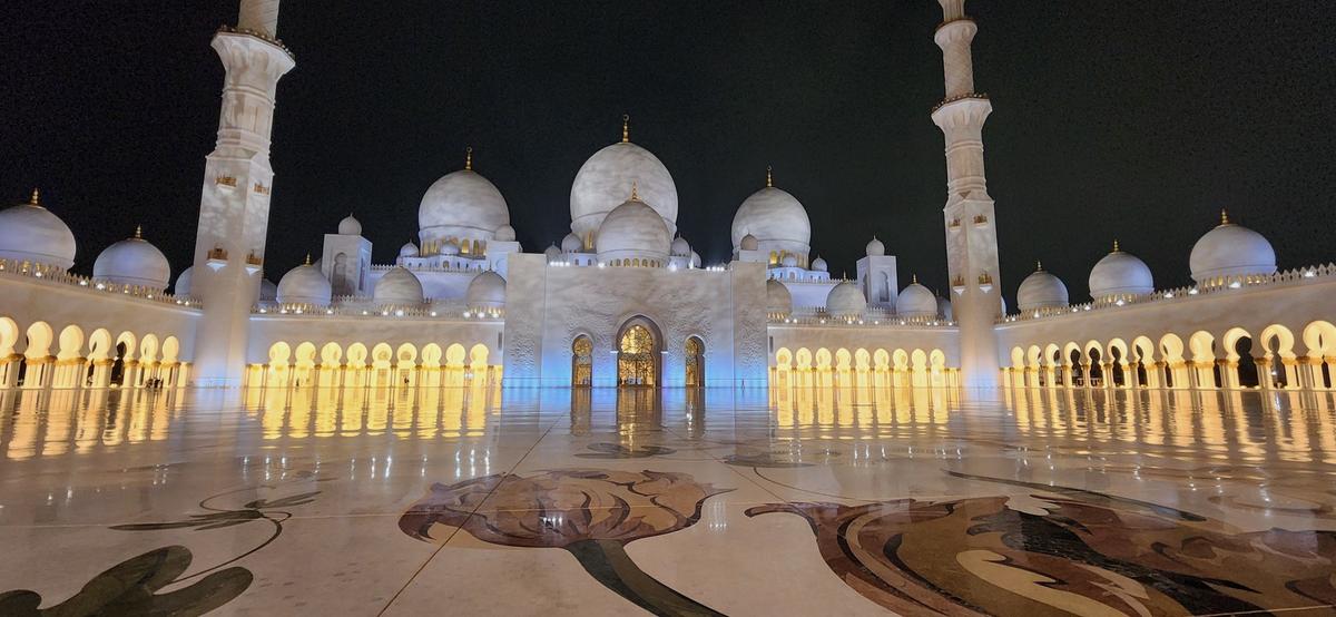Sheikh Zayed Grand Mosque, a nighttime photo of the impressively large building featuring white marble domes and towers.