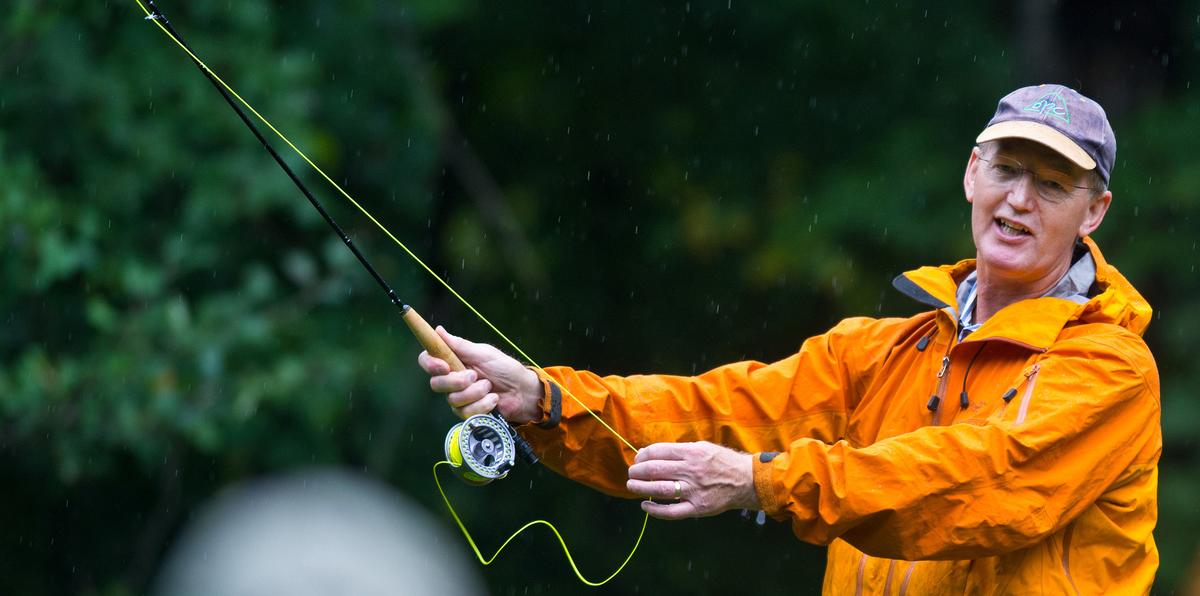 Man in orange rain coat demonstrating fly-fishing technique