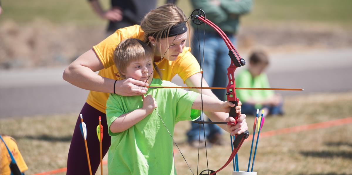 woman showing a young boy how to use a bow and arrrow