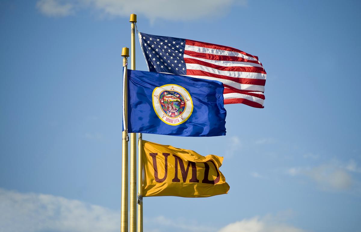 3 flags in the wind: United States of America, Minnesota, and UMD.
