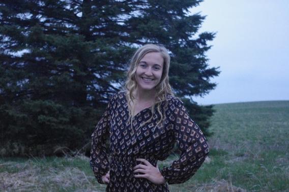 Ashley Miller, outside in front of an evergreen tree, smiling