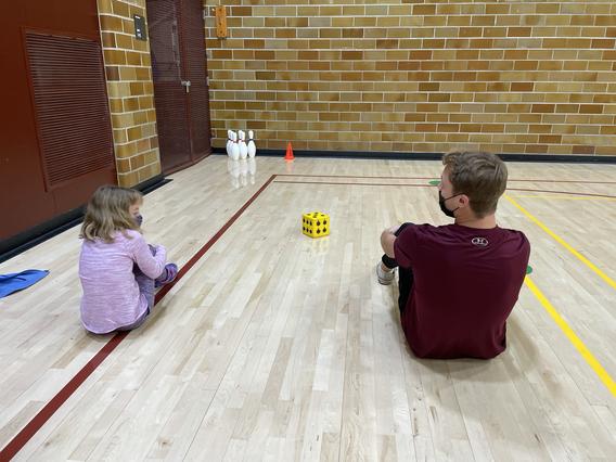Child and instructor sitting down side by side with their knees up, facing each other 