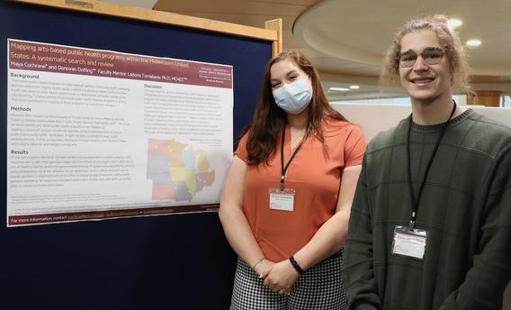 Two public health students standing in front of a poster