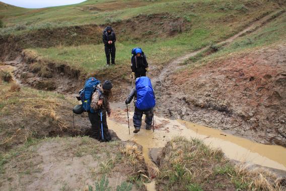 A group of students wearing hiking gear traversing through the mud in the Badlands of North Dakota