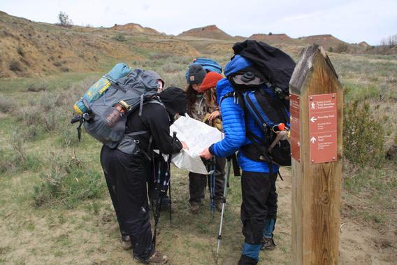 A group of students wearing hiking gear navigating through the Badlands of South Dakota while all reading a map huddled in a group