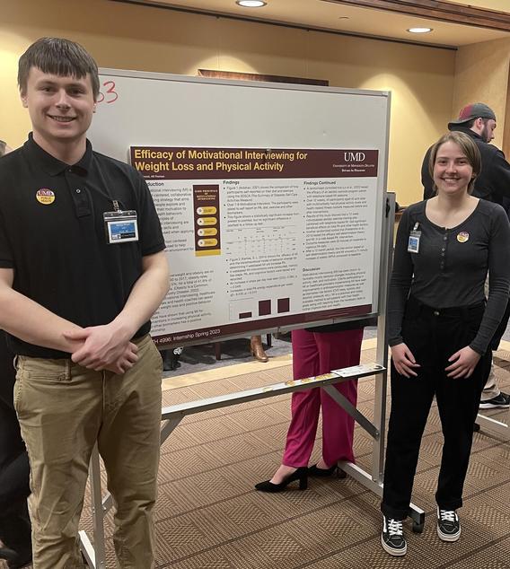 Grant Mrozek and Alli Pearson standing next to a research poster, smiling 