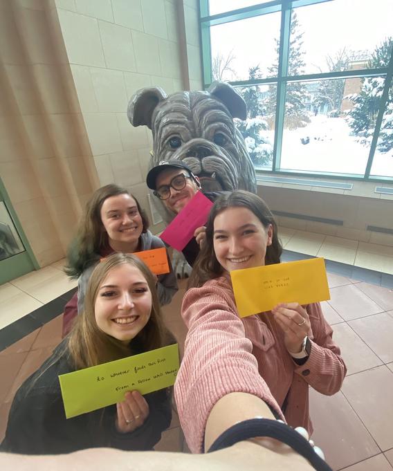 Four students holding up positive affirmation notes posing near Champ statue.  