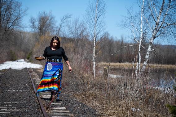 Ariana Northbird carrying a basket and walking along the railroad tracks near the water