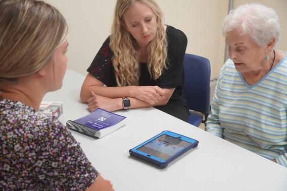 Two young women assisting an older woman looking at an iPad