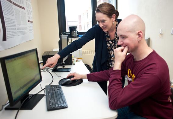 A faculty member points out something on a computer monitor to a student.