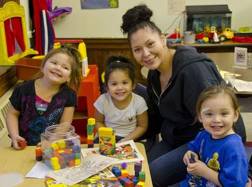 Woman and 3 kids in a daycare smile for the camera