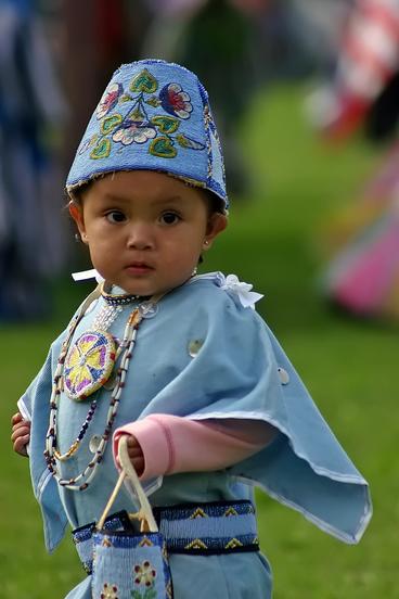 American Indian child dressed in pale blue, beaded hat and top