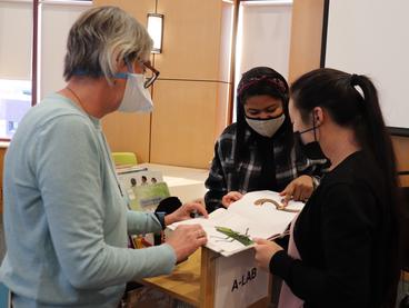 A professor with two students, masked, looking at children's books