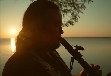 profile of person playing flute with sunset in the background